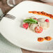 A Tuxton white square coupe pasta plate with ravioli and tomatoes on it.