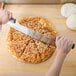 A hand using an American Metalcraft double handle pizza rocker knife to cut a slice of pizza.