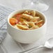 A Tuxton eggshell china soup cup filled with chicken noodle soup.