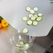 A person using a WebstaurantStore flexible cutting board to slice a cucumber over a bowl of peppers.