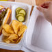 A hand holding a white styrofoam container with food.