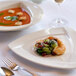 A Tuxton white triangle china plate with shrimp and grapes on a table.