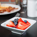 A white Tuxton mini footed square china bowl filled with strawberries and blueberries.