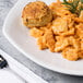 A Tuxton white square china pasta plate with macaroni and cheese and a biscuit on a table with a fork and spoon on a white napkin.