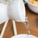 A white jug pouring water into a white GET Porcelain Fuji Sake Bottle.