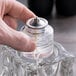 A hand holding a glass jar with a Sterno candle fuel cartridge inside.