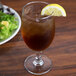 An Arcoroc Excalibur goblet of brown liquid with a lemon wedge on top.