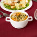 A bowl of soup with vegetables and bread in an Arcoroc white double handled bowl on a table.