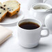 A white Arcoroc tall cup filled with brown liquid on a saucer with a plate of bread.