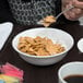 A person eating cereal with milk from a white Arcoroc glass bowl using a metal spoon.