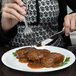 A woman using a fork and knife to eat meatballs on an Arcoroc white glass plate.