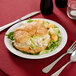 A plate with a croissant sandwich, salad, and fruit on it.