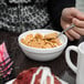 A person eating cereal in a white Arcoroc glass bowl with a spoon.