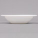 An Arcoroc white opal glass bowl with a rim on a gray surface.