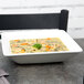 A Tuxton bright white square china bowl filled with soup and vegetables on a table.