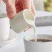 A person pouring milk into a Tuxton eggshell china creamer.