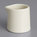 A Tuxton eggshell white ceramic creamer on a gray surface.