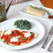 A Tuxton porcelain white china pizza plate with flatbread, sauce, and cheese on a table with a fork and knife.