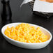 A Tuxton oval white china baker filled with macaroni and cheese on a table with a basket of bread.