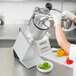 A woman using a Hobart continuous feed food processor to slice green peppers.