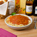 A white Tuxton pasta bowl filled with spaghetti and sauce on a table with wine bottles.