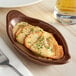 A Tuxton oval mahogany rarebit dish on a table with a plate of Welsh rarebit.