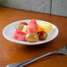 A Tuxton porcelain white china mini pasta bowl filled with fruit on a table with a fork and knife.