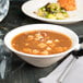A Tuxton eggshell china bowl filled with soup next to a plate of food.