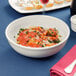 A Tuxton eggshell china bowl of pasta with sauce on a table with a glass of wine.