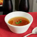 A Tuxton porcelain white soup bowl filled with broth and topped with a leafy green leaf.