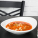 A Tuxton porcelain oval bowl filled with soup, noodles, and vegetables on a table.