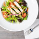 A close up of a salad with chicken and vegetables in a Tuxton white bowl.