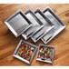 A group of rectangular American Metalcraft hammered stainless steel trays with salad on them.