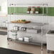 A stainless steel table with two chrome wire undershelves and two chrome wire overshelves, used for kitchen storage and prep.