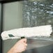 A hand using a Unger green and white StripWasher to clean a window.