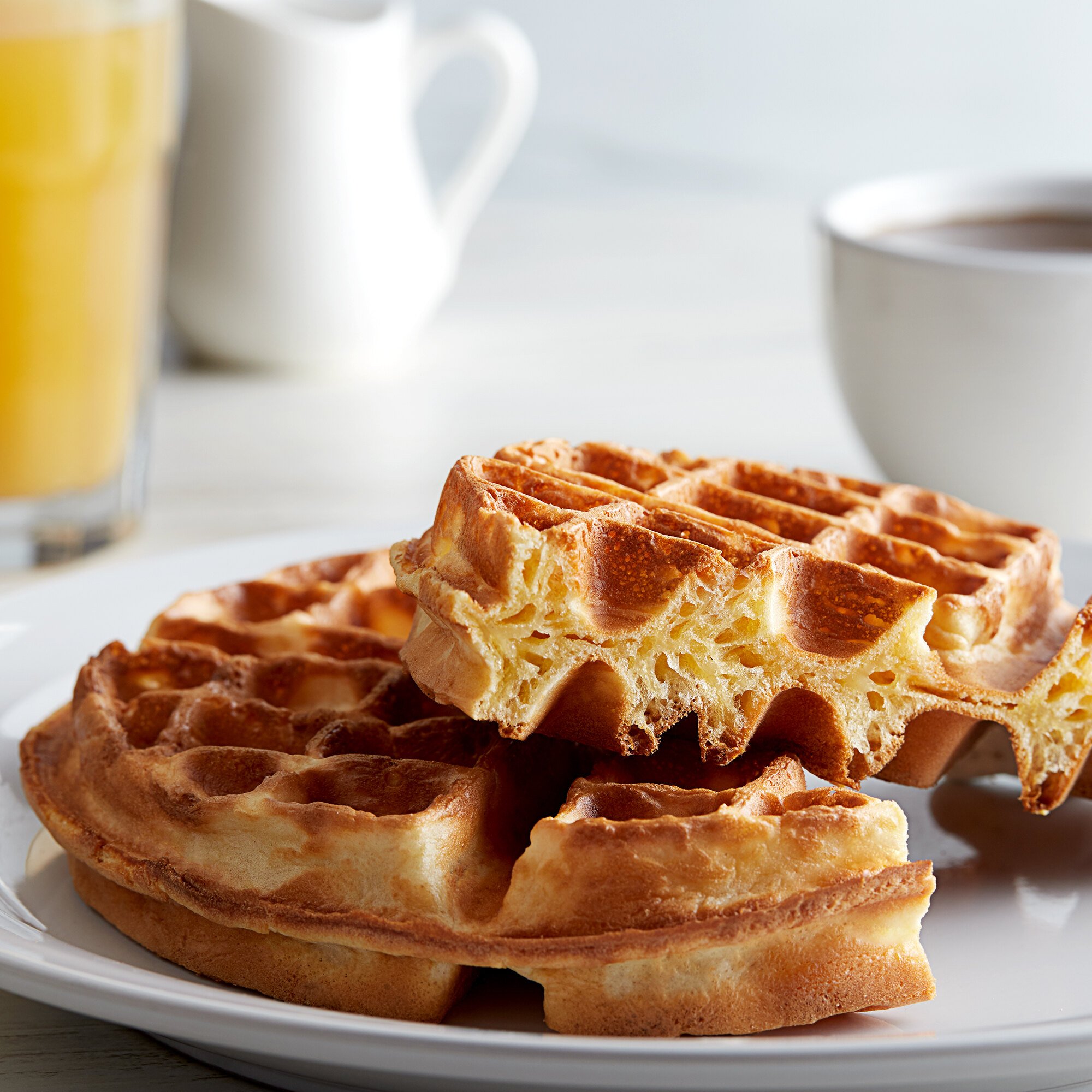Two belgian waffles on white plate in front of glass or orange juice and cup of coffee