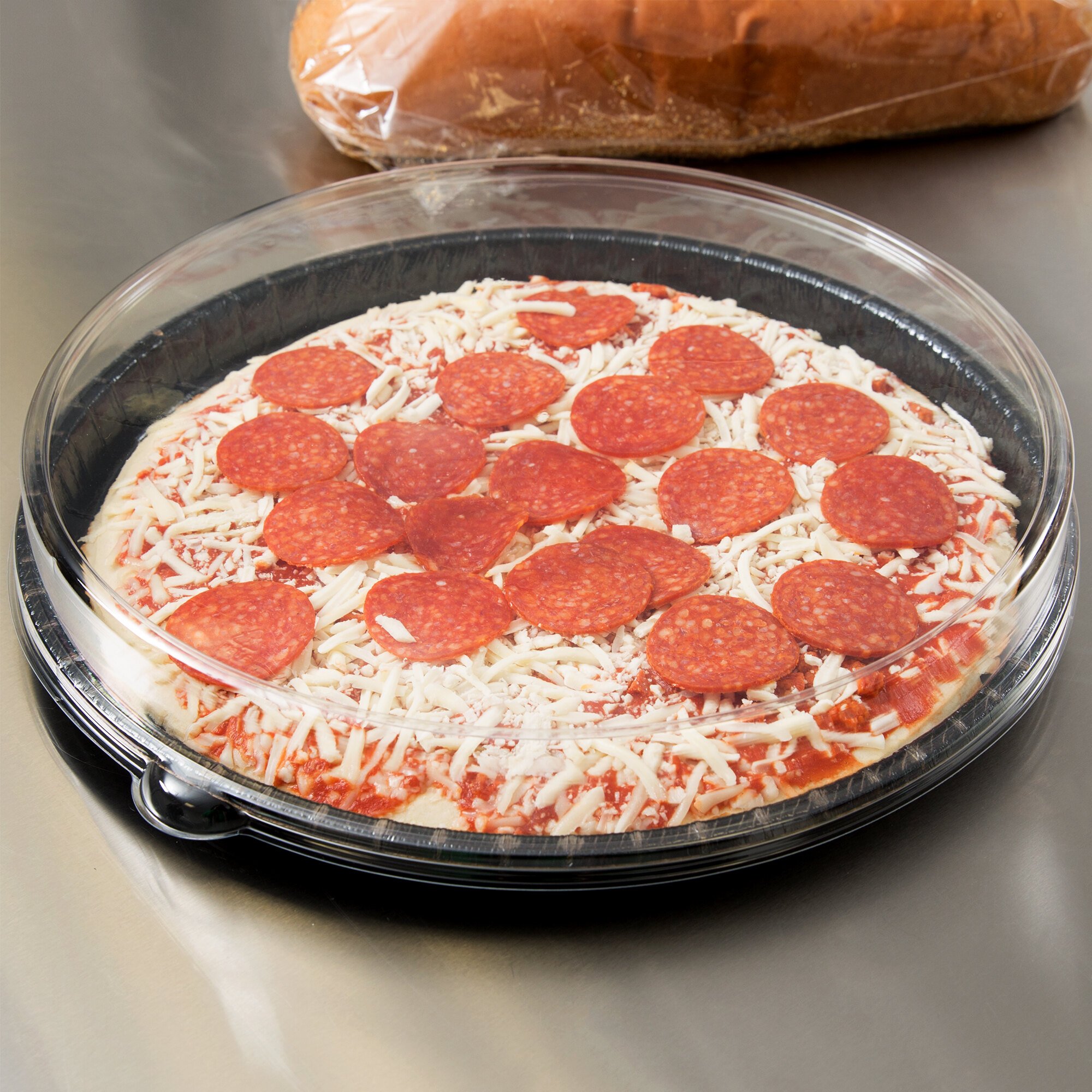 Black plastic tray with lid containing an unbaked pizza