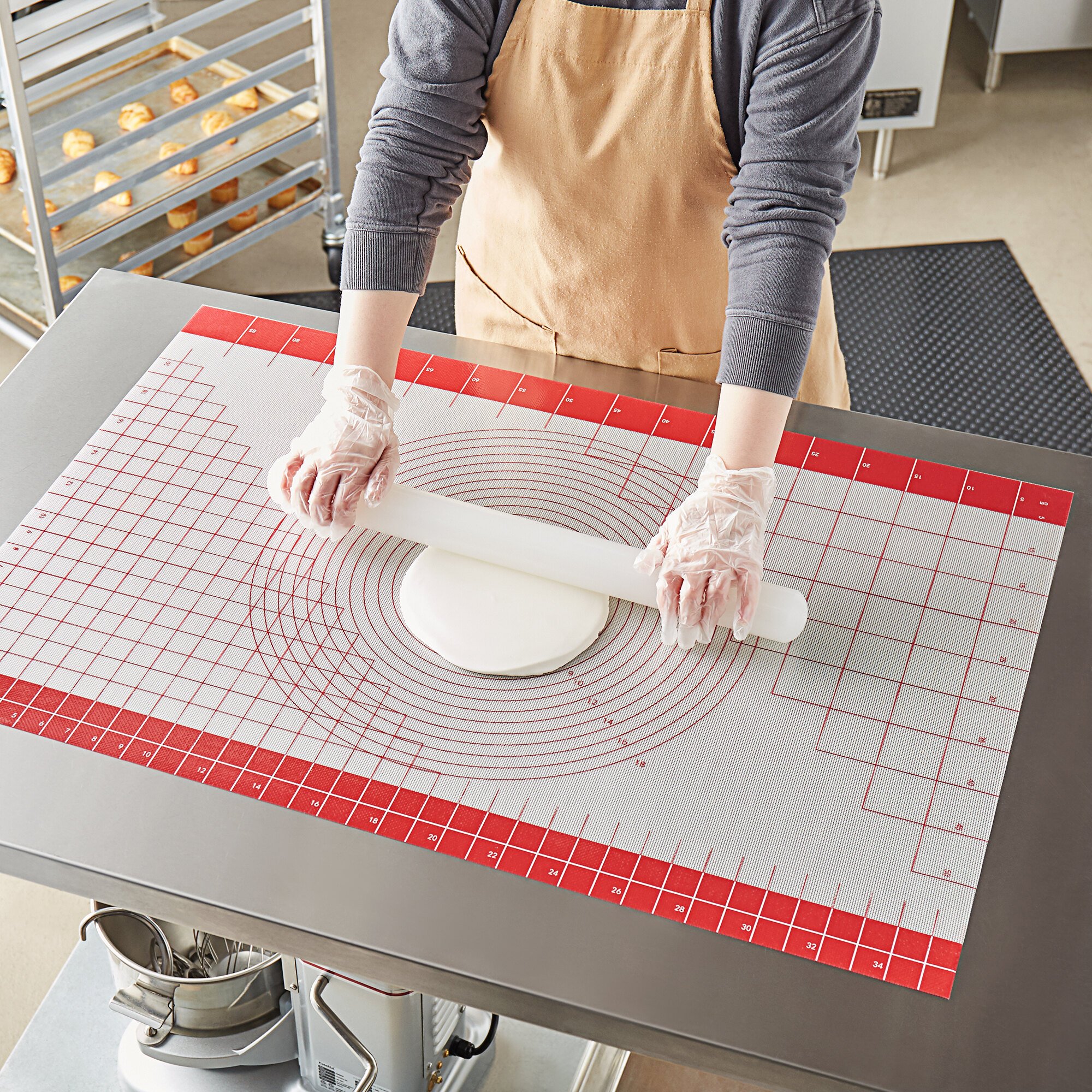 A person rolling out cake fondant on a baking mat.
