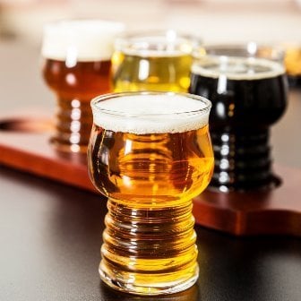 hard cider in glass with three glasses of beer on a wooden paddle behind it