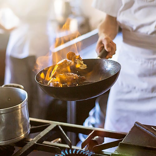 Chef sauteing a pan of food with flames rising from the pan