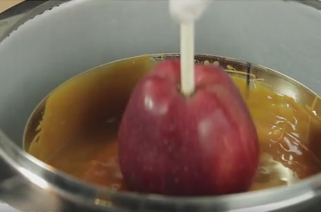 apple with skewer dipping into melted caramel