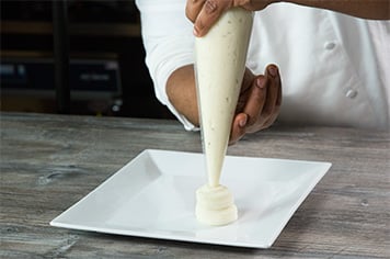 A chef pipes potatoes onto a white square plate