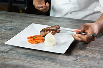A chef plates a steak with precision tongs