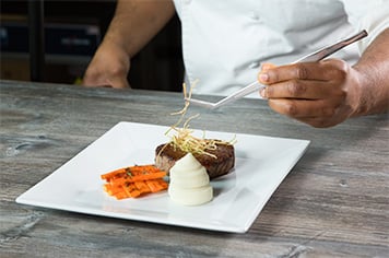 Using precision tongs, a chef garnishes a steak