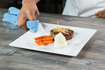 After plating his meal, a chef wipes the edges of his plate down with a clean towel for a clean presentation
