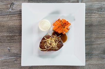Steak, fried leeks, whipped potatoes, and carrots plated in the classic food presentation style