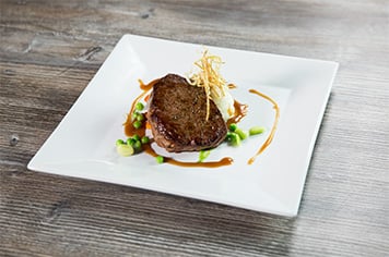 a chef using fried leek shoestrings to garnish a steak