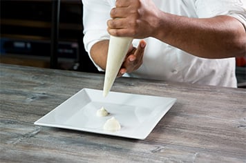 A chef pipes dots of potato puree onto a plate using a pastry bag
