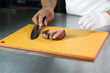 A chef slices a steak into three pieces using a chef's knife