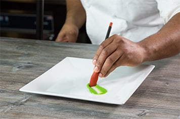 a chef brushing sauce onto a white plate